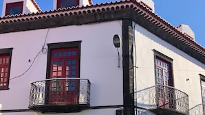 A white building with red doors and windows, a balcony with a metal railing, and a street in front. - The Farm - Azores Boutique House (Ponta Delgada)