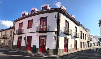 Un edificio de dos pisos con puertas y ventanas rojas, paredes blancas y balcones con barandillas de metal.