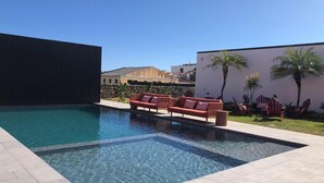A swimming pool with clear water, surrounded by a tiled deck. There are red lounge chairs and a stone wall in the background. - The Farm - Azores Boutique House (Ponta Delgada)
