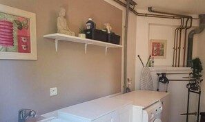 A laundry area with a washing machine, a drying rack, and a shelf with toiletries.