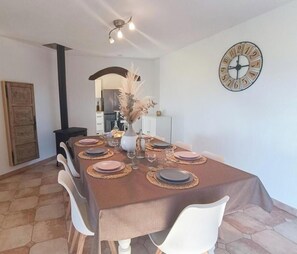 Een eethoek met een tafel voor vier personen, een klok aan de muur en een decoratieve vaas met gedroogde bloemen.
