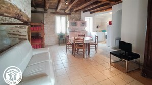 A cozy room with a white sofa, wooden dining table, and chairs. A television is on a stand in the corner. - Gîtes de France® - L'Oustal (SAINT-SOZY)