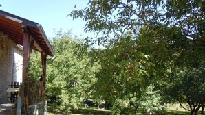 A rustic building with a wooden porch, surrounded by lush greenery and trees. - Gîtes de France® - L'Oustal (SAINT-SOZY)