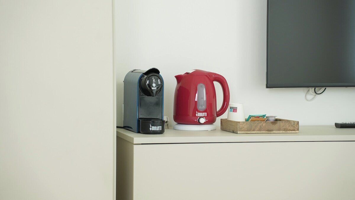 A kitchenette with a coffee maker, a red kettle, a remote control, and a box of tissues on a counter.