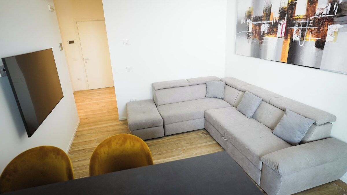 Un salon moderne avec un canapé d’angle gris, un téléviseur à écran plat fixé au mur et un plancher en bois.