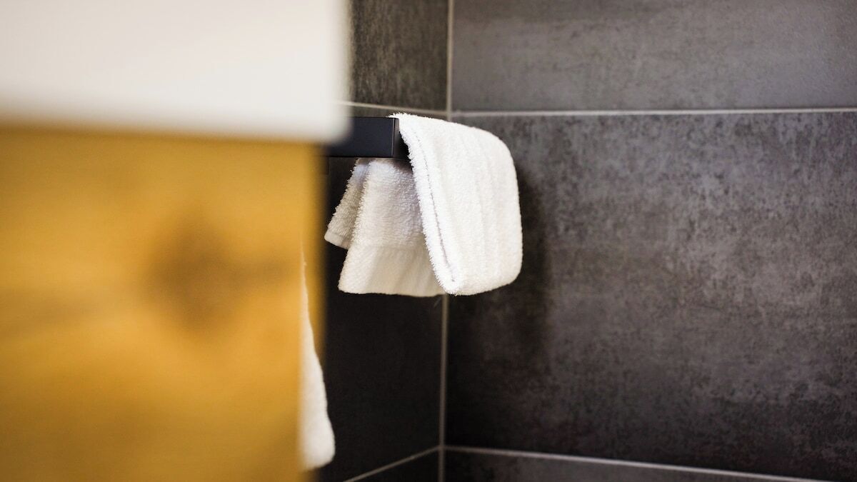 Un baño con paredes de azulejos oscuros y un perchero con una toalla blanca.