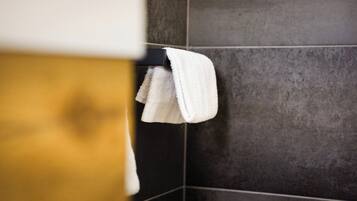 Un baño con paredes de azulejos oscuros y un perchero con una toalla blanca.
