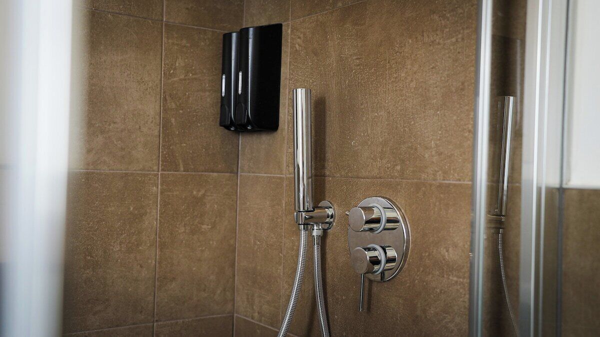 A shower area with a handheld showerhead and a wall-mounted control panel.