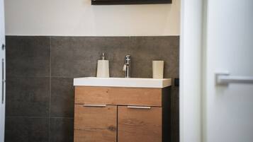 A bathroom with a white sink, two soap dispensers, and a wooden cabinet with drawers.