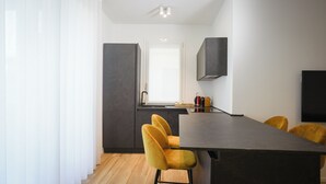 Une cuisine moderne avec un plan de travail foncé, une fenêtre et un four encastré. On y trouve deux chaises jaunes et une table noire.