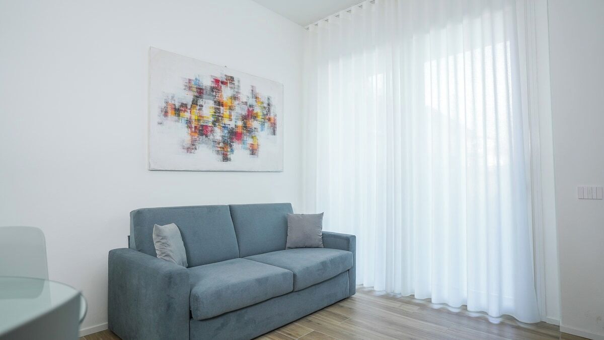 A living room with a grey sofa, a glass table, and a colorful abstract painting on the wall.