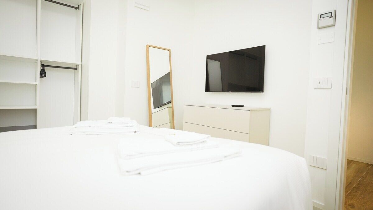 A hotel room with a bed, a TV mounted on the wall, a mirror, and a wardrobe.