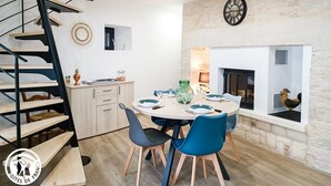 A modern kitchen with a dining area, a spiral staircase, and a stone wall. - Gîtes de France® - Le Gîte d'Inès (THEDIRAC)