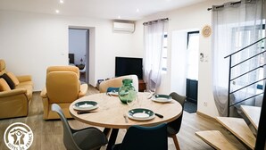 A modern living room with a round dining table set for two, a sofa, and a TV. - Gîtes de France® - Le Gîte d'Inès (THEDIRAC)