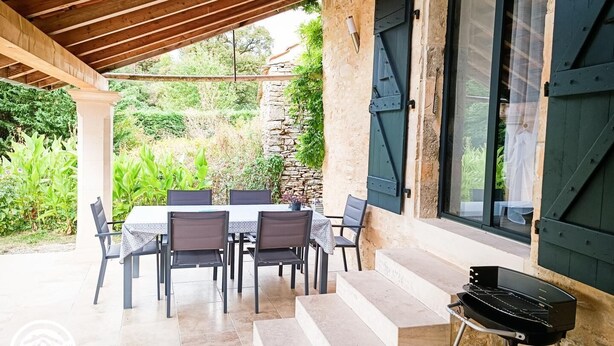 An outdoor patio with a table and chairs, a grill, and a stone wall. - Gîtes de France® - Le Gîte d'Inès (THEDIRAC)