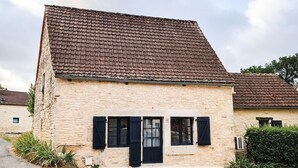 A two-story stone building with a tiled roof, a central entrance with black shutters, and a gravel driveway. - Gîtes de France® - Le Gîte d'Inès (THEDIRAC)