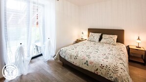 A bedroom with a large bed, two bedside tables with lamps, sheer curtains, and a ceiling light fixture. - Gîtes de France® - Le Gîte d'Inès (THEDIRAC)