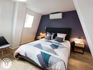 Un dormitorio con cama, dos mesitas de noche, una silla y un equipo de aire acondicionado en la pared.