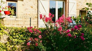 Ein Steinhaus mit weißen Fensterläden, einem Fenster und einem Garten mit rosa Blumen.