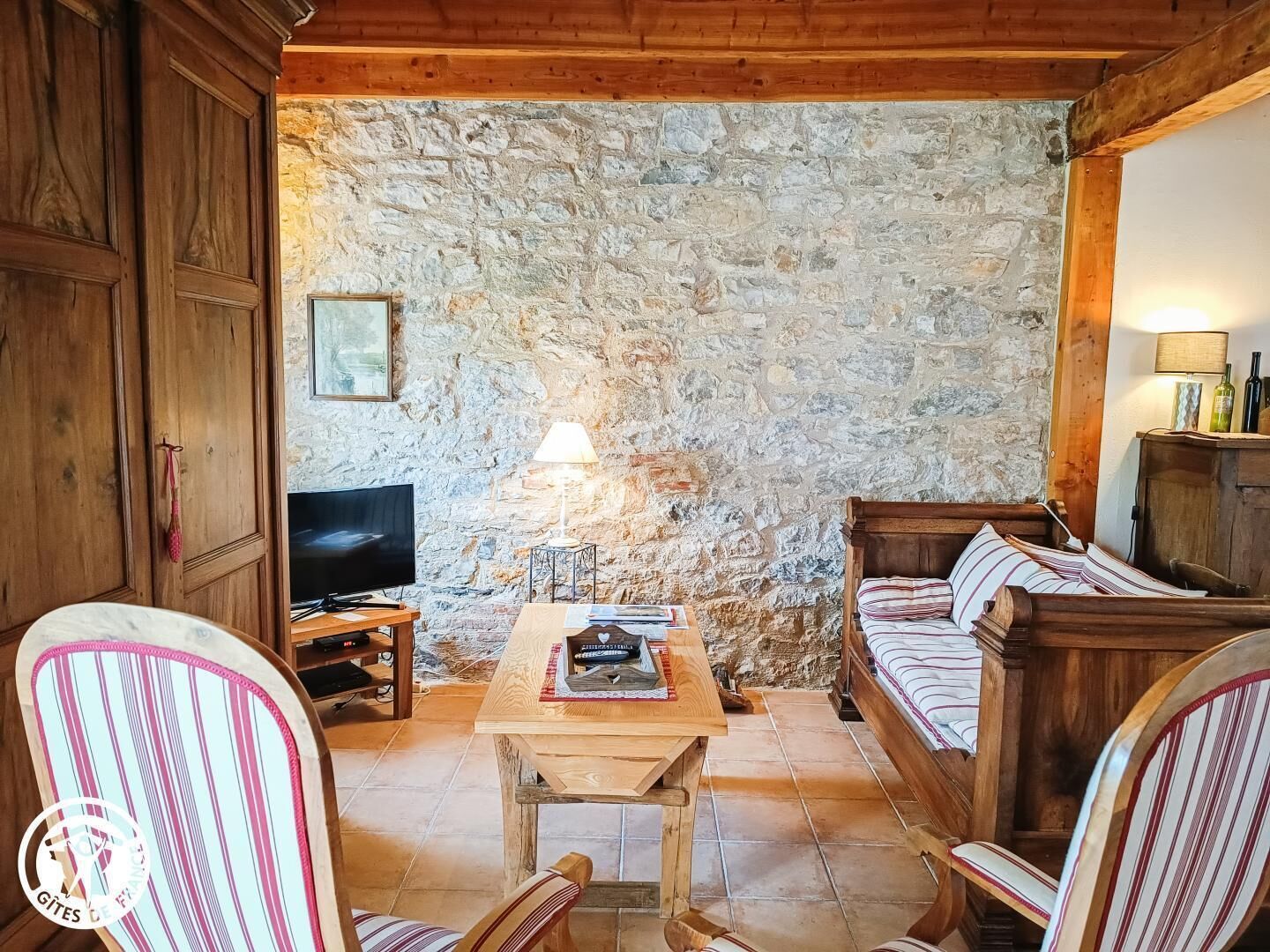 Una habitación rústica con pared de piedra, muebles de madera, un televisor y una lámpara.