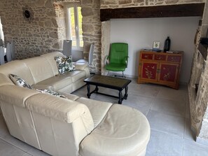A living room with a beige sofa, a green chair, a wooden cabinet, and a stone wall.