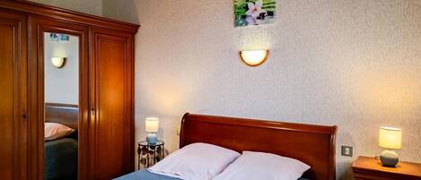 Une chambre à coucher avec un lit en bois, deux lampes de chevet, un luminaire fixé au mur et un miroir.