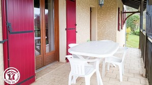 Une terrasse couverte avec une table et des chaises blanches, des portes rouges et une lanterne suspendue.