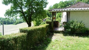 Une petite maison avec un toit en tuiles, une véranda et une haie bien entretenue.