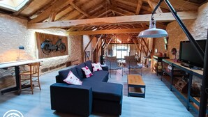 Una habitación rústica estilo loft con vigas de madera a la vista, un sofá seccional negro, una mesa de comedor y un televisor.