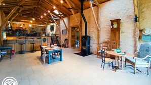 Un interior rústico con vigas de madera a la vista, una mesa central con sillas, una zona de cocina y una pared de piedra.
