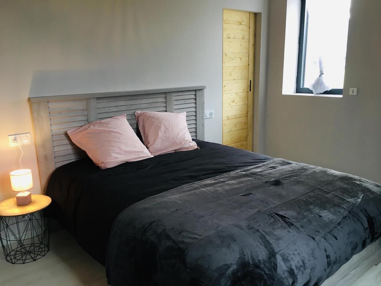 A bedroom with a bed, two pillows, a bedside lamp, and a window.