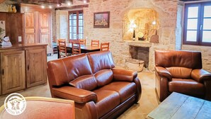 A rustic interior with a stone wall, wooden furniture, a leather sofa, and a fireplace.