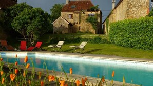 A poolside area with lounge chairs, a stone building, and a well-maintained lawn.