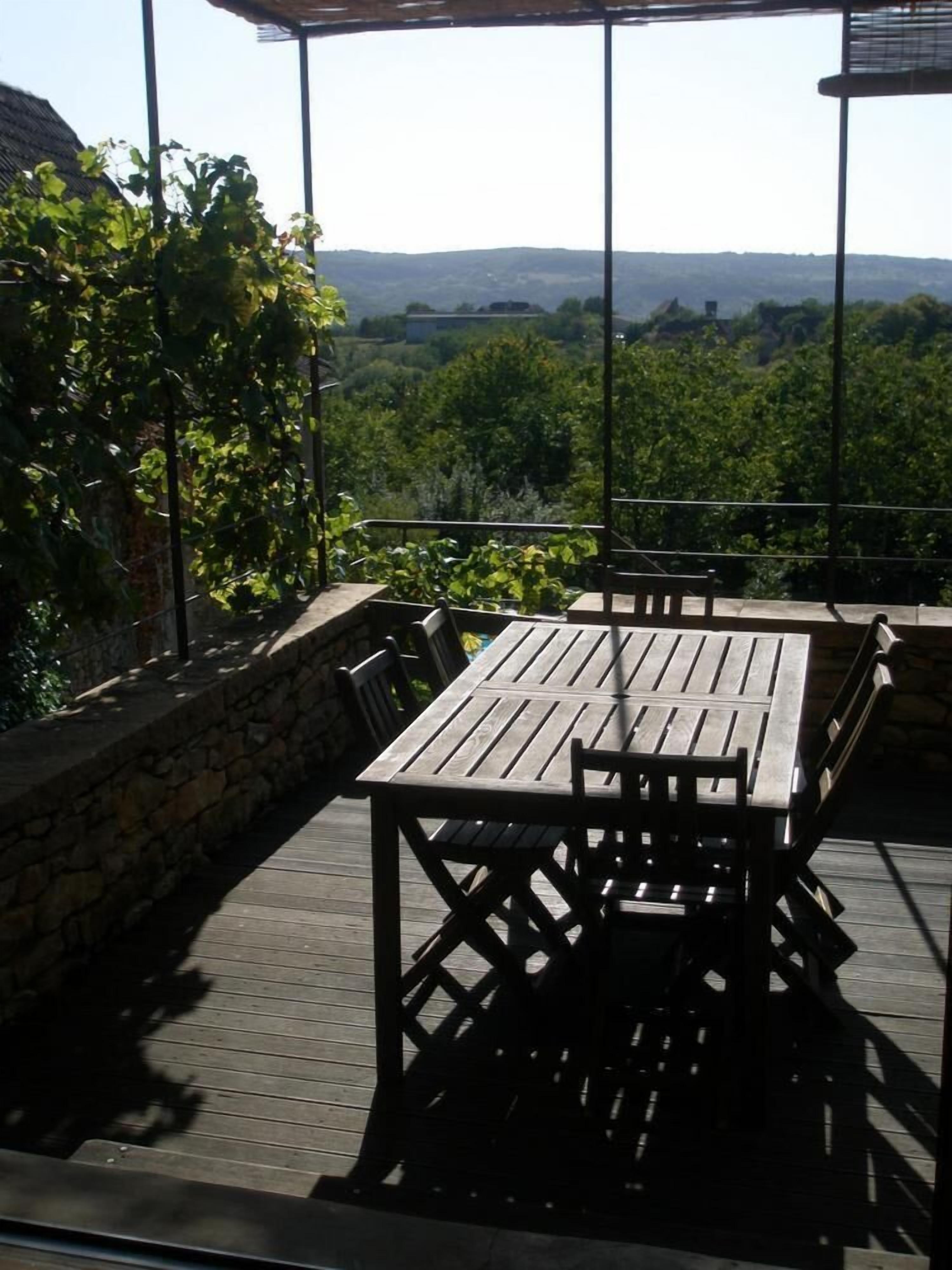 Un patio exterior con una mesa y sillas de madera, rodeado de muros de piedra y vistas a un paisaje exuberante.