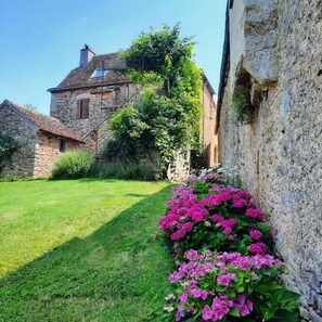 Experience the tranquil charm of this traditional stone building, surrounded by a lush garden with vibrant flowers.