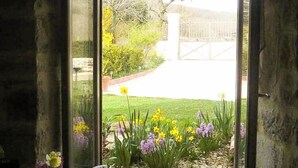 A window seat with a cushion, overlooking a garden with flowers and a pathway.
