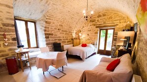 A cozy room with a stone wall, a bed, a sofa, a table with chairs, and a small dining area.