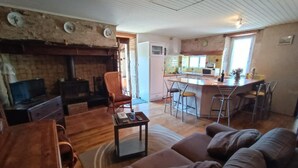 A living room with a fireplace, wooden furniture, a kitchen area with bar stools, and a dining table.