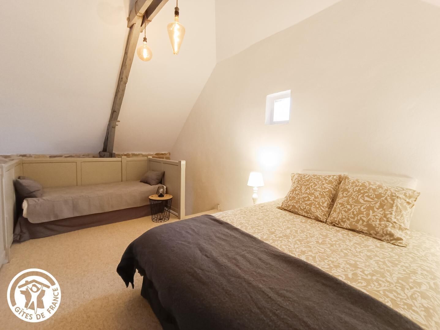 Une chambre confortable et bien éclairée, située sous les toits, avec un lit, un coin salon et une petite table.