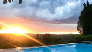 Piscina com vista para o pôr do sol sobre uma paisagem montanhosa.