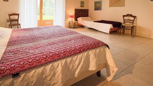 Una habitación con una cama grande, una cama más pequeña, una silla, una mesita de noche y una ventana con cortinas.