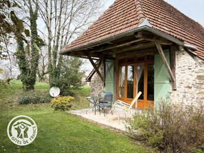 A stone cottage with a tiled roof, a covered porch, and a small patio with outdoor furniture. - ROSALIE - BANNES - Vacation Rental (BANNES)