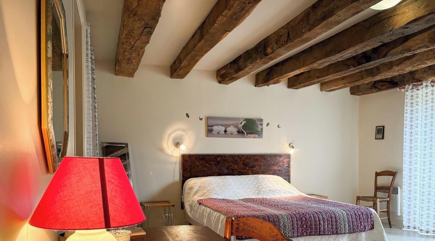 Een slaapkamer met een houten plafond, een bed met een beddengoed met een patroon, een rode lamp en een aan de muur hangend schilderij.