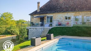 Una casa de piedra con piscina, mobiliario exterior y una escalera que conduce a la entrada.