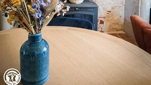 Una habitación rústica con pared de piedra, techo de vigas de madera, un jarrón azul con flores secas y un cuadro en la pared.