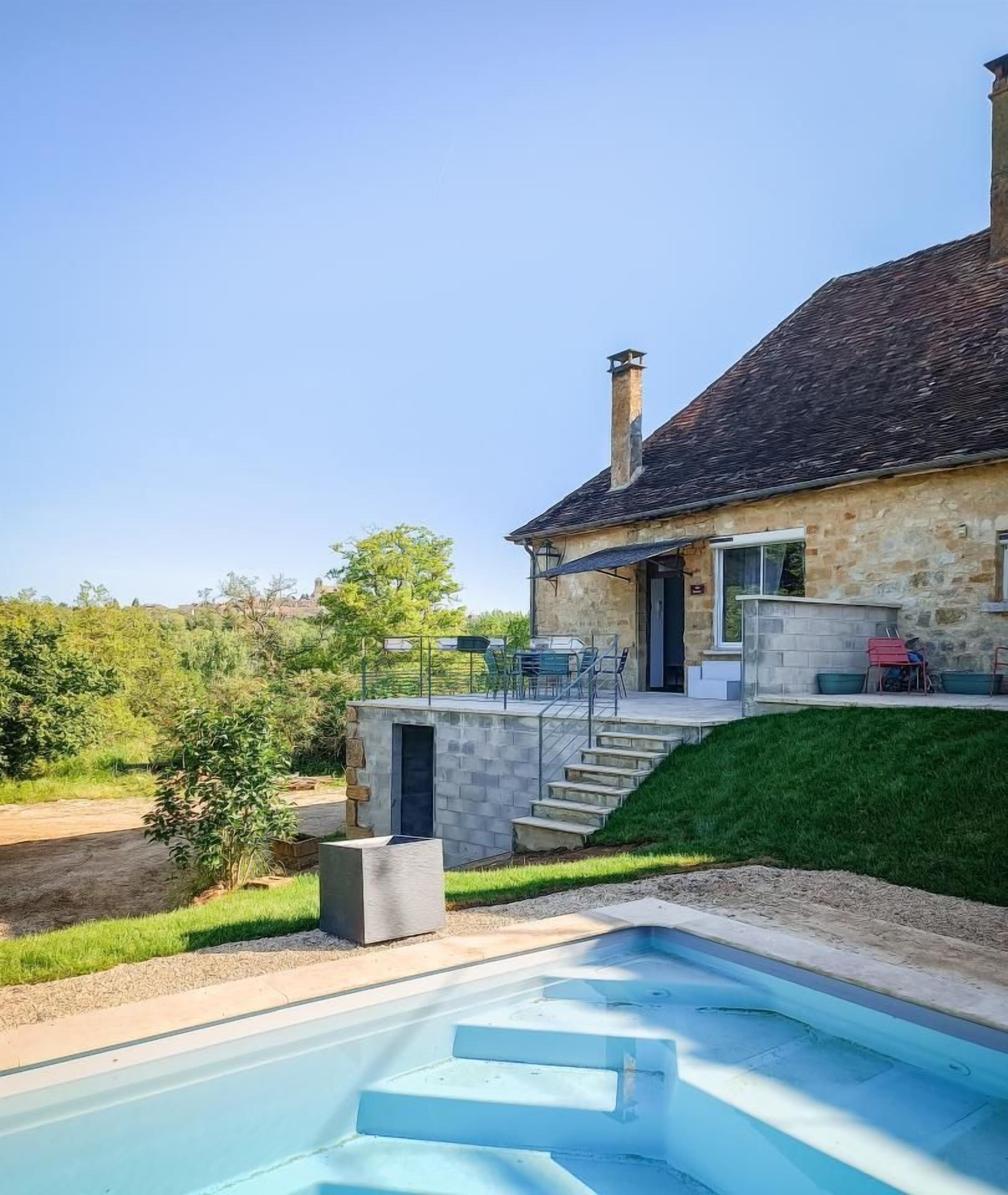 Une maison en pierre avec une piscine, un patio couvert et un escalier menant à une terrasse.