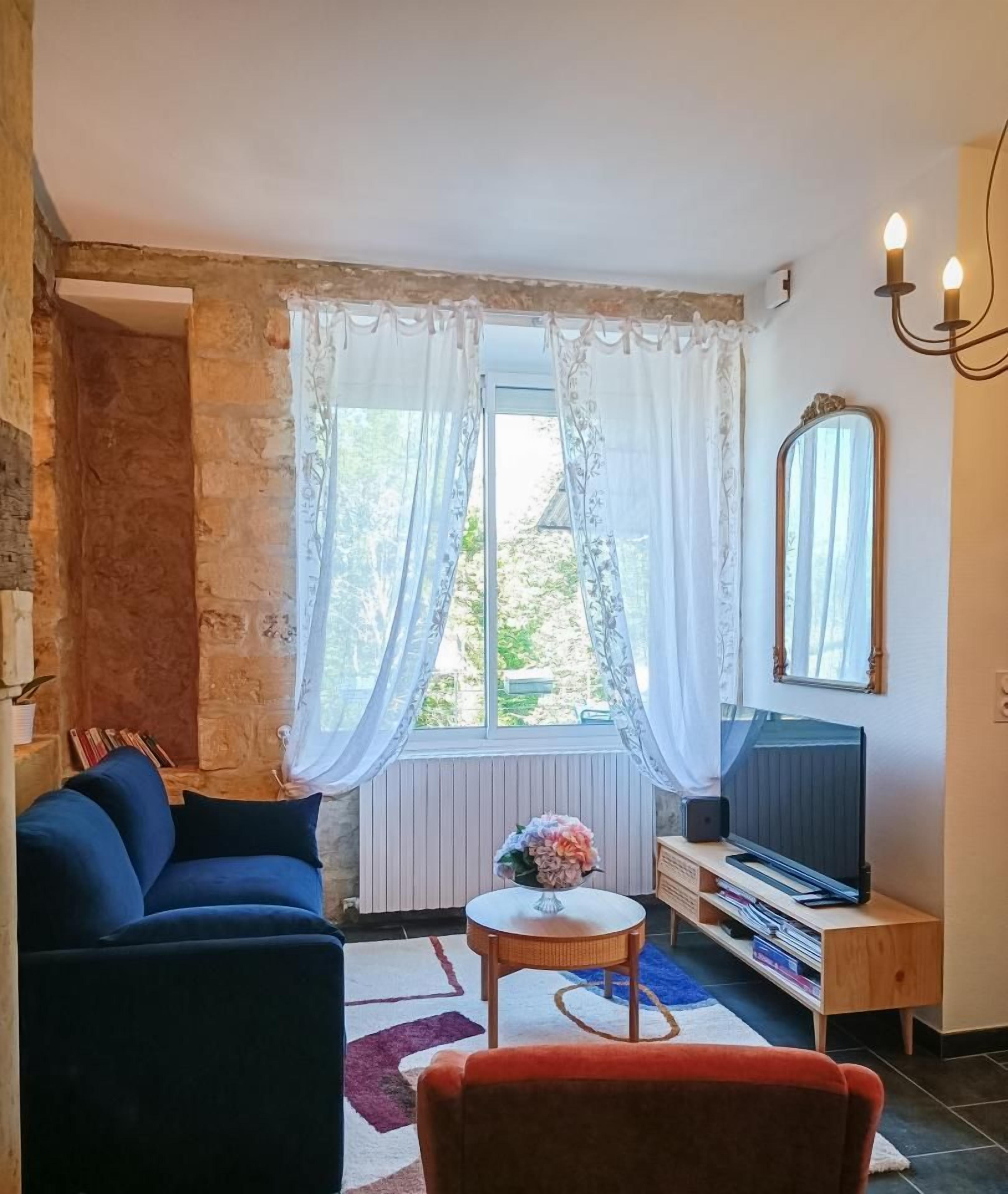 Una sala de estar con un sofá azul, una silla roja, un televisor y una ventana con cortinas.