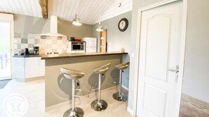A modern kitchen with a white countertop, a microwave, a coffee maker, and a clock on the wall. There are three bar stools in front of the counter.