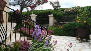 A stone staircase leading to a gated entrance, surrounded by flowering plants and a tree. - Gîtes de France® - La Cigale (SAINT PROJET)