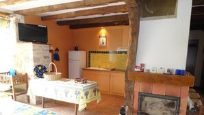 Een gezellige kamer met een open haard, een televisie, een kitchenette en een eettafel met tafelkleed.